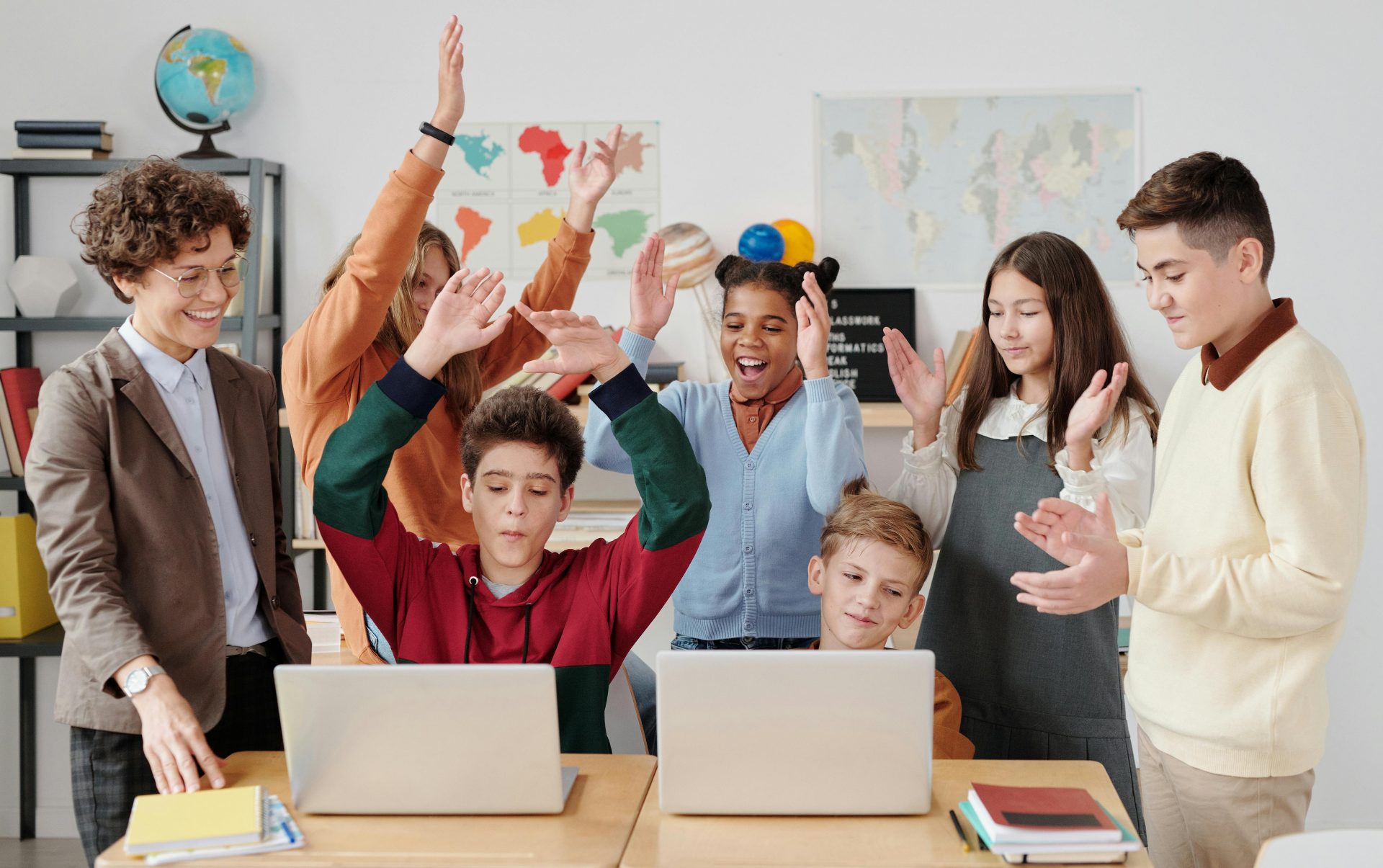 A group of happy students and a teacher clapping together in a school classroom.