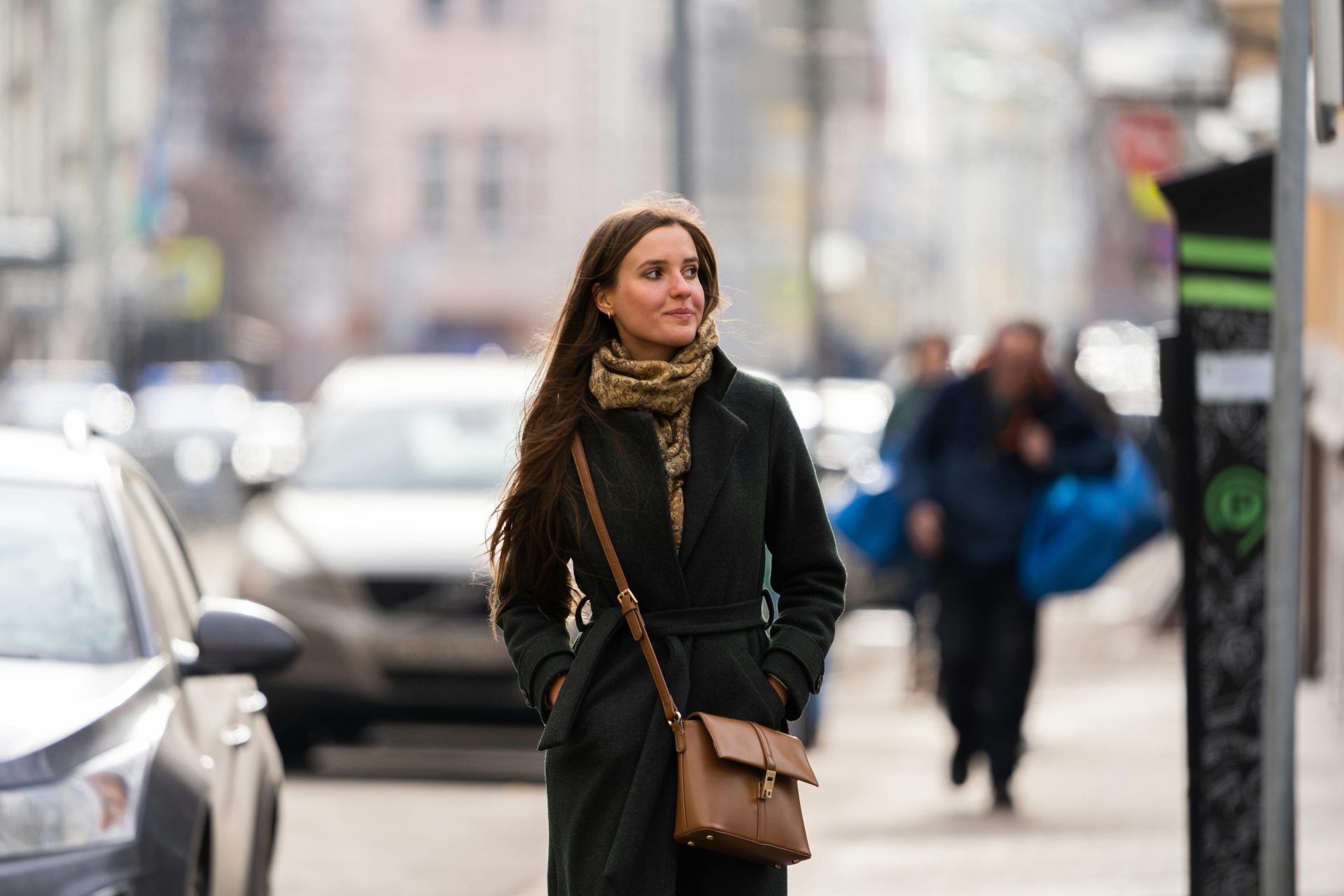 Elegant woman in a black coat walking through Moscow's bustling streets with a scarf and sling bag.