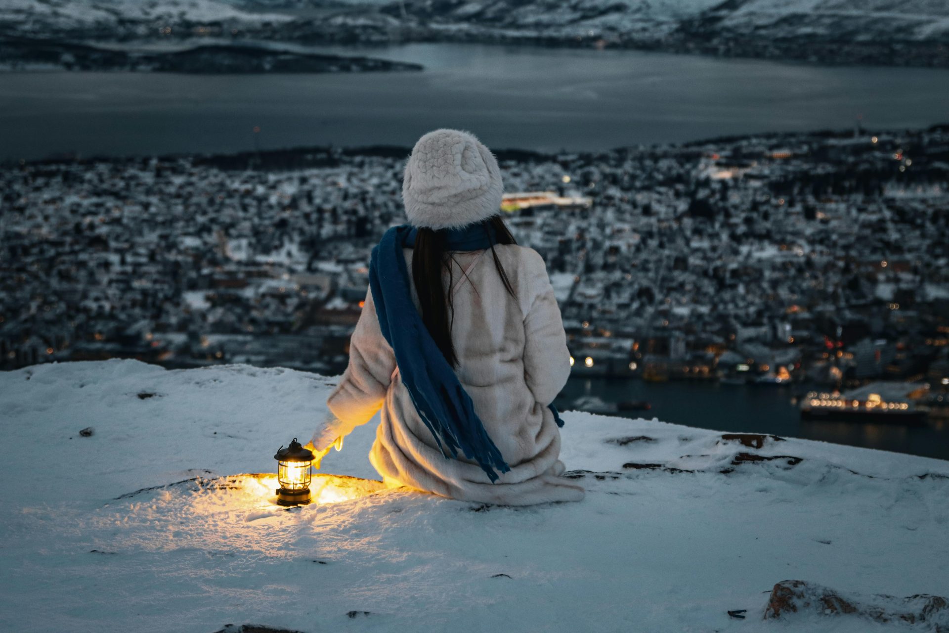 Woman with lantern overlooking snowy Tromsø. Peaceful night scene.