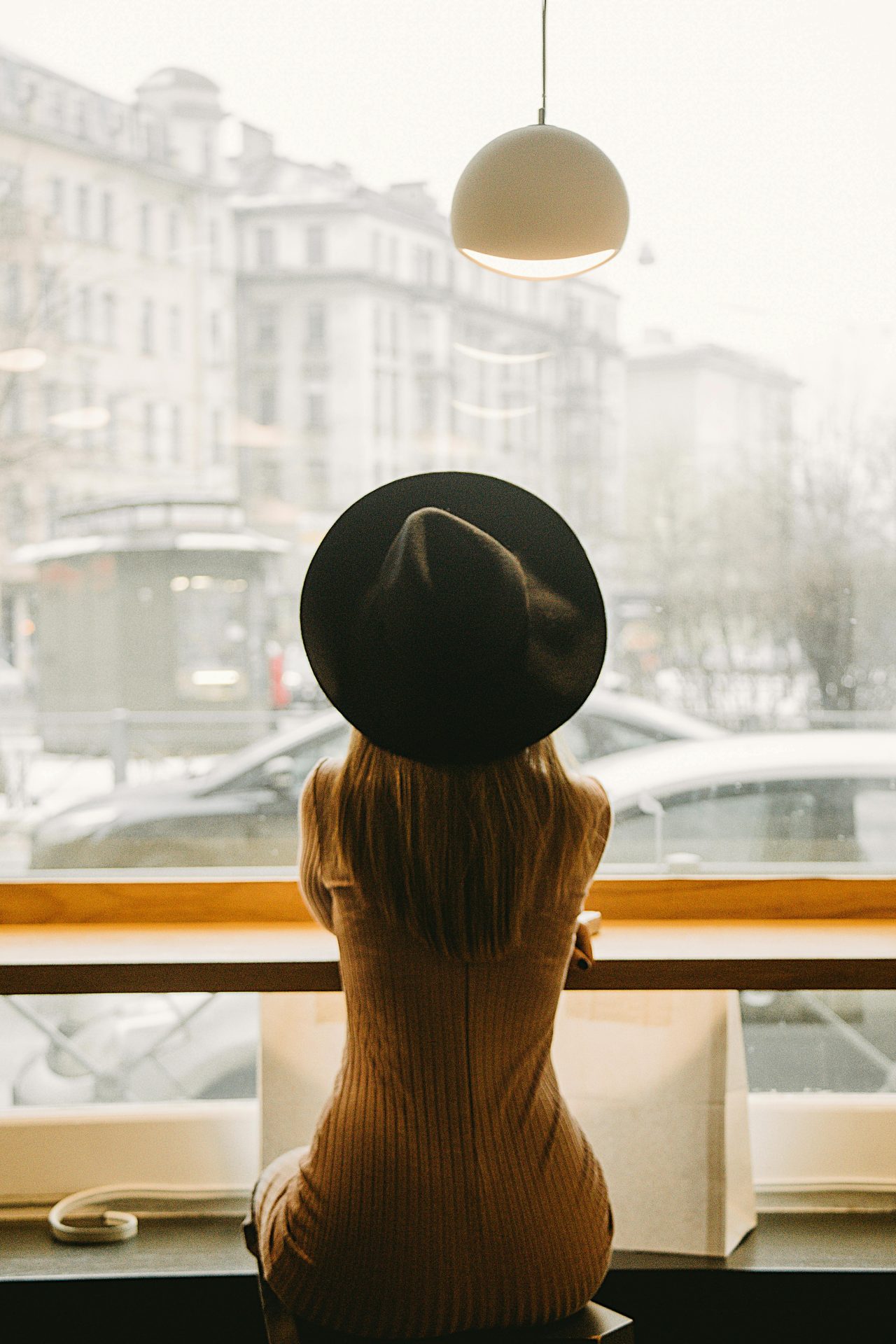 Stylish woman in a hat sits in a café, gazing outside at a bustling St. Petersburg street.